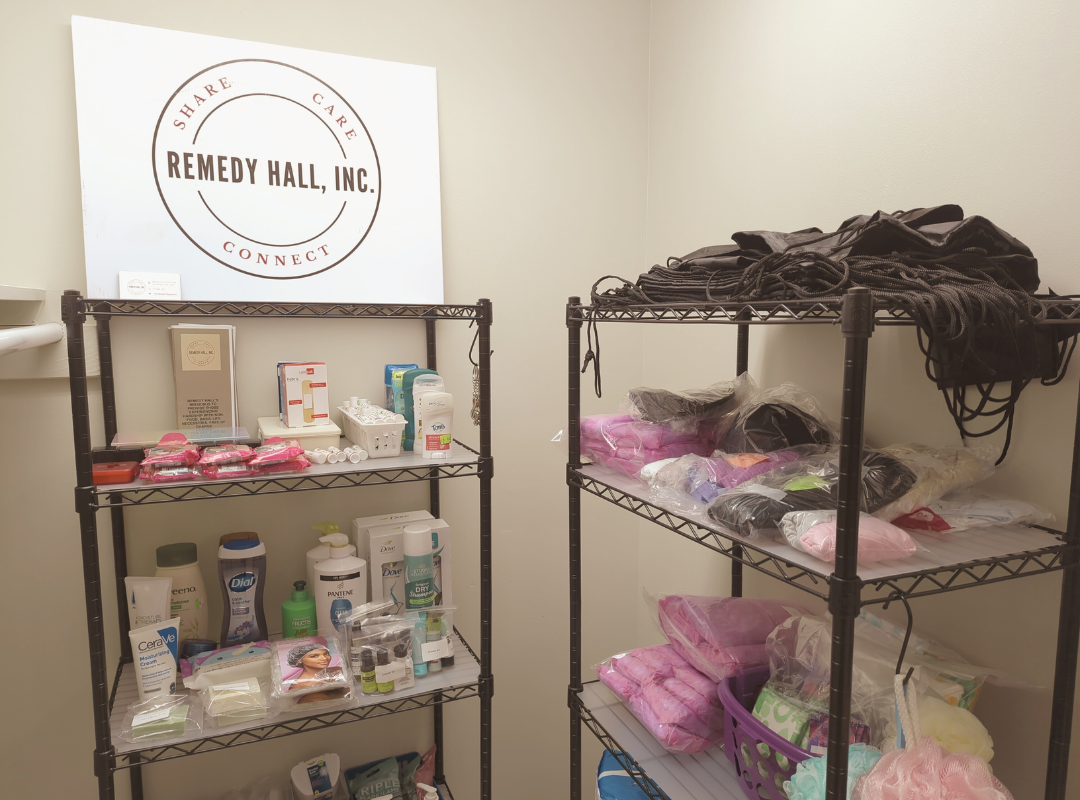 A photograph of our new satellite station for Remedy Hall in the library, showing a corner with shelving containing essential items free for taking.
