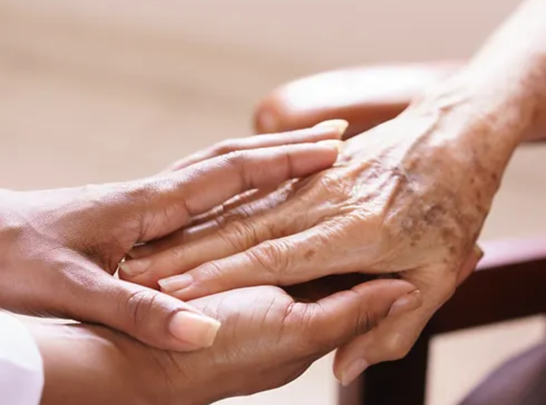Close-up photograph of a younger person holding the hand of an older person.