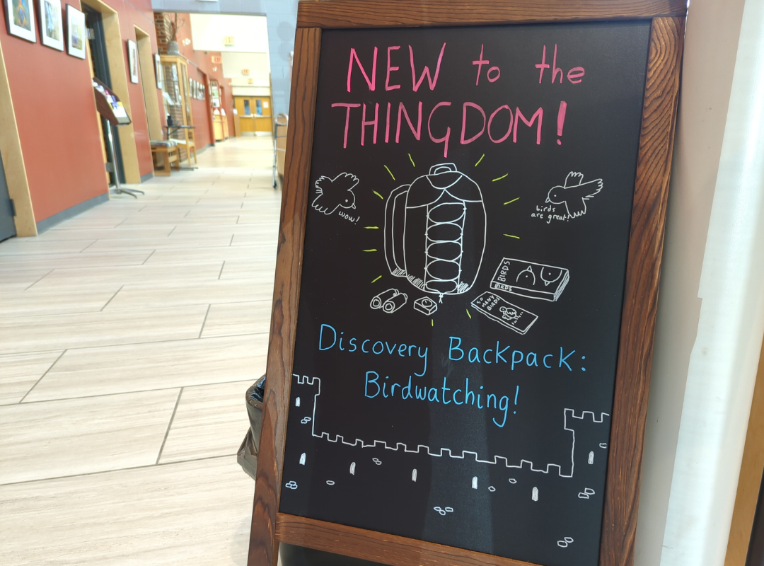 A chalkboard in the library announcing the addition of a birdwatching Discovery Backpack to the library's Thingdom (library of things)