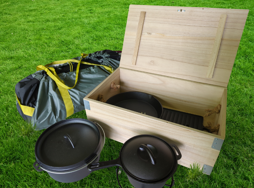 Image shows a tent in its bag, alongside a wooden box containing cast iron cookware