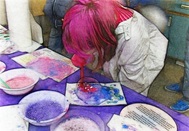 Photo of girl with pink hair leaning over blowing colored bubbles on paper