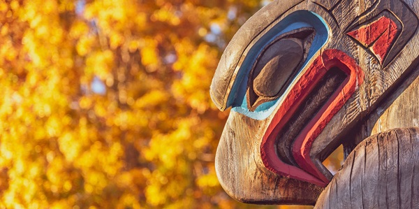 An eagle at the top of a totem pole with golden fall leaves in the background.