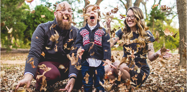 A mom, dad, and son, enjoying playing in the fall leaves and throwing them up in the air.