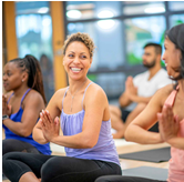 A woman dressed in workout attire, smiling while attending a yoga class. The event link this image will take you to will open in an external site and in a new tab or window.