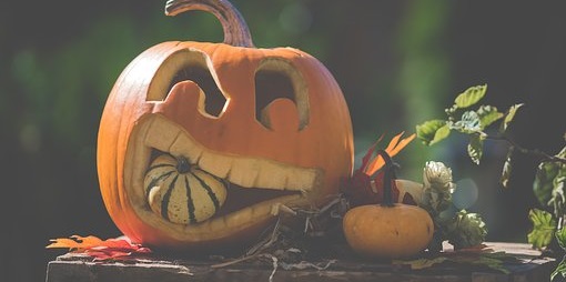 A large pumpkin cut into a jak o'lantern. The "mouth" of the jak o'lantern has a smaller squash/goard in it and appears to be biting down on it.