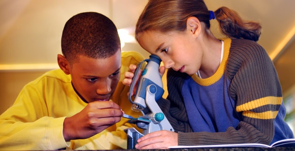 An eleven year old girl and 11 or 12 year old boy taking turns looking through a microscope.